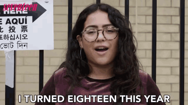a woman wearing glasses is standing in front of a sign that says i turned eighteen this year