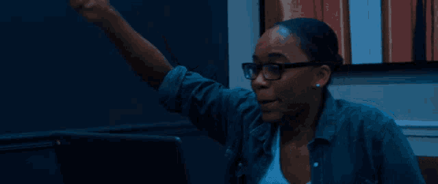a woman wearing glasses is pointing at something in the dark