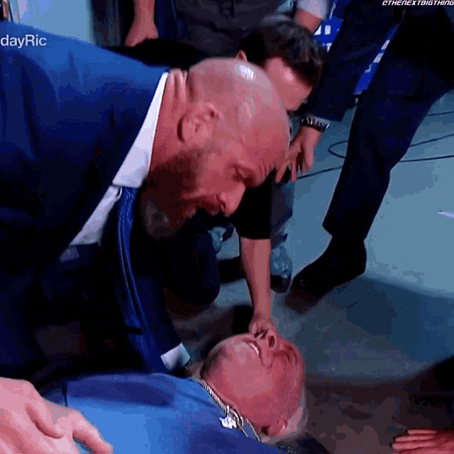 a man in a suit is kneeling down next to a man in a blue shirt who is laying on the ground