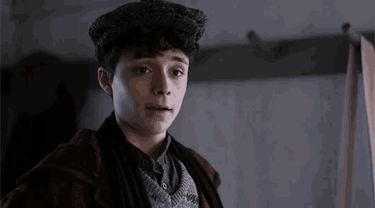 a young boy wearing a hat and a jacket is standing in a room .