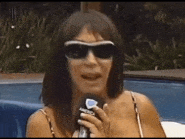 a woman wearing sunglasses is holding a microphone and talking into it .