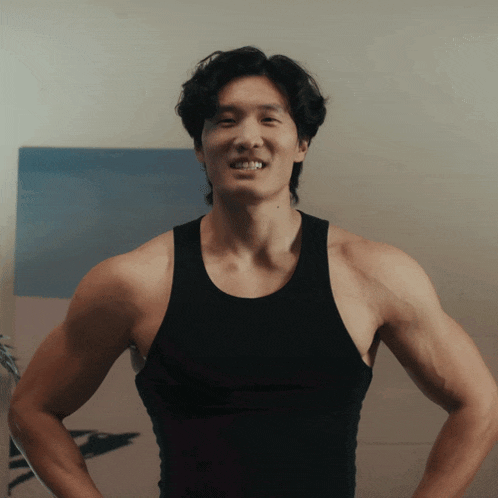 a man in a black tank top stands with his arms crossed