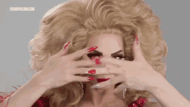 a drag queen with red nails is applying makeup to her face .