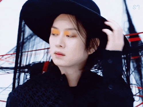 a woman wearing a black hat and orange eyeshadow