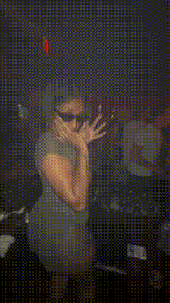 a woman wearing sunglasses and a gray dress is kneeling down in a dark room