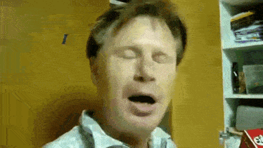a man is yawning with his eyes closed in front of a shelf .
