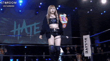 a woman in a wrestling ring holding a championship belt with the word hate behind her