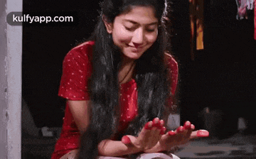 a woman in a red dress is sitting on the ground with her hands in her lap .