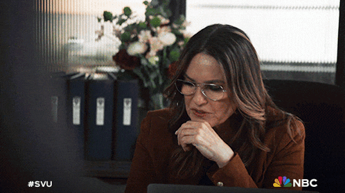 a woman wearing glasses sits at a desk in front of a laptop with the nbc logo in the corner