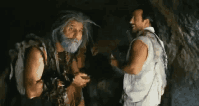 two men are standing next to each other in a cave and one has a beard .