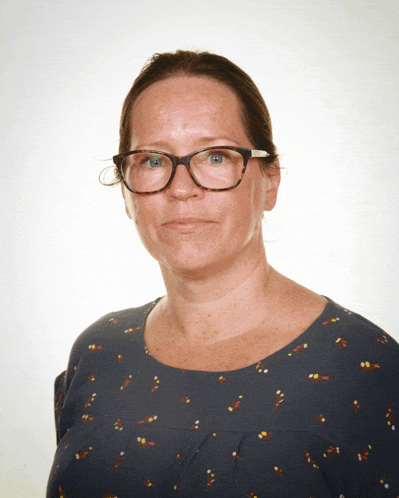 a woman wearing glasses and a blue shirt looks at the camera with a serious look on her face