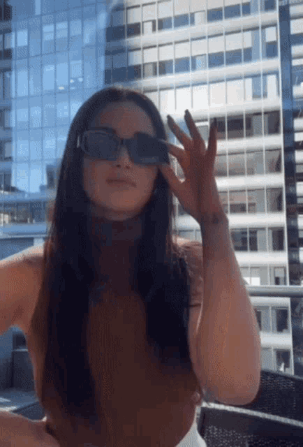 a woman wearing sunglasses is standing in front of a tall building