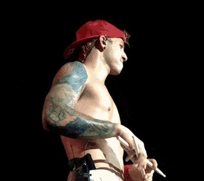 a shirtless man with tattoos on his arms is holding a microphone and a cigarette .