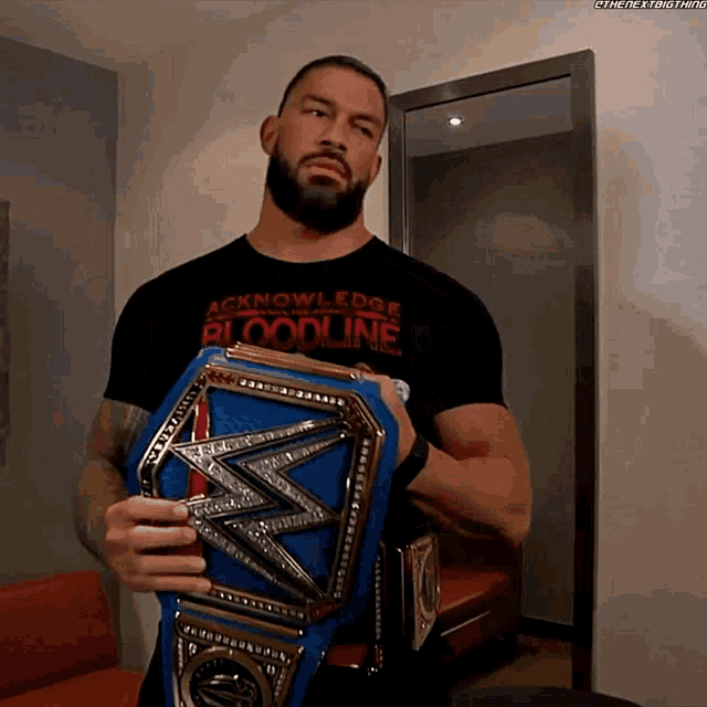 a man in a black shirt that says acknowledge bloodline is holding a wrestling belt