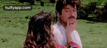 a man and a woman are standing next to each other in a field with their eyes closed .