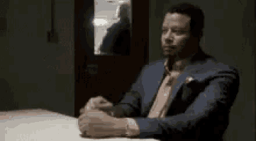 a man in a suit and tie is sitting at a table with his arms crossed