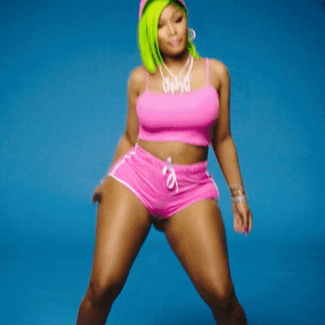 a woman with green hair wears a pink top and shorts