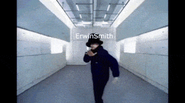 a man in a black top hat is dancing in a hallway with erwinsmith written on the wall behind him