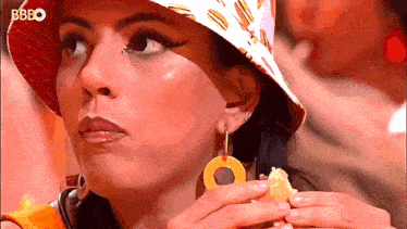 a woman wearing a hat with hamburgers on it eating a sandwich