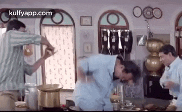 a group of men are standing around a table in a kitchen fighting each other .