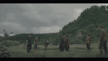 a group of men are standing in a grassy field with a windmill in the background
