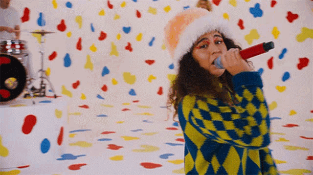 a woman singing into a microphone in front of a wall with colorful confetti