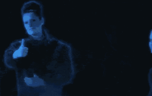 a man and a woman are giving a thumbs up in a dark room .