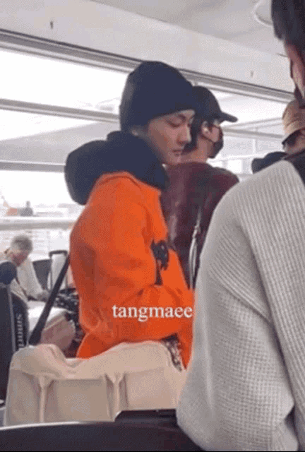 a man wearing an orange jacket and a black beanie is sitting next to a woman wearing a white sweater and a white bag