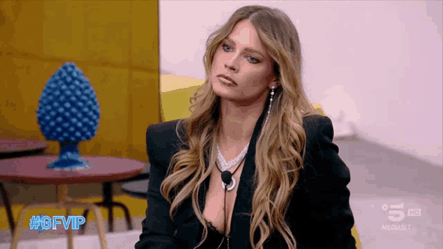 a woman wearing a black jacket and a plunging neckline is sitting in front of a table that says #gfvip