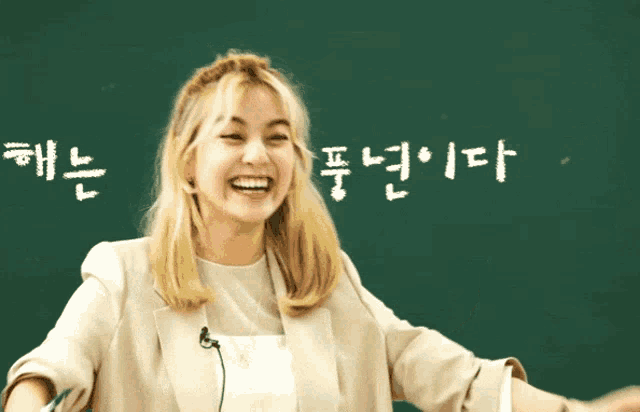 a woman laughs in front of a blackboard with korean writing