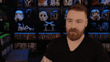 a man with a tattoo on his arm is sitting in front of a shelf full of storm trooper helmets
