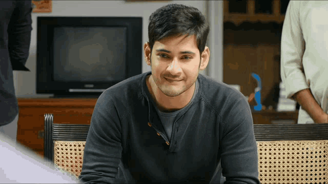a man in a black sweater sits in front of a television