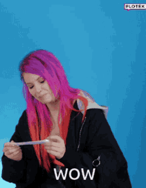 a woman with purple and red hair is holding a piece of paper and says wow