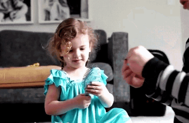a little girl in a blue dress is brushing her hair with a brush