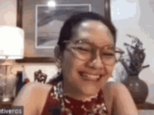 a woman wearing glasses is smiling and looking at the camera while sitting at a table .
