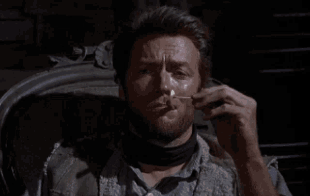 a man with a beard is sitting in a chair lighting a cigarette