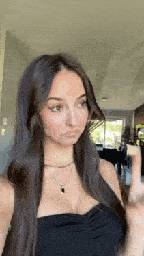a woman in a black top and necklace is making a funny face .