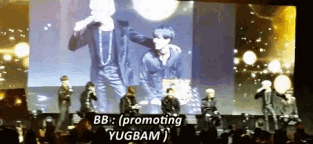 a group of men are standing on a stage in front of a large screen with the words `` promoting yugbam '' on it .