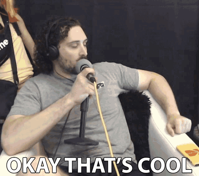 a man wearing headphones is singing into a microphone with the words okay that 's cool behind him