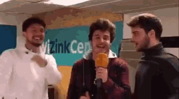 three young men are standing next to each other in a room . one of the men is holding a microphone and smiling .