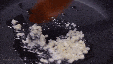 garlic is being cooked in a pan with a wooden spoon in it .