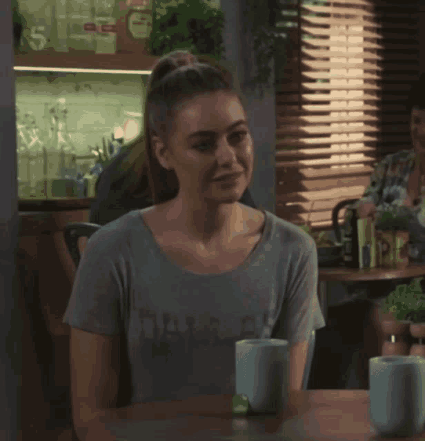 a woman wearing a grey shirt that says dazzler sits at a table with two mugs