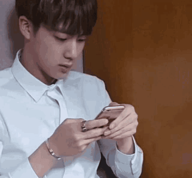 a young man in a white shirt and tie is looking at his phone .