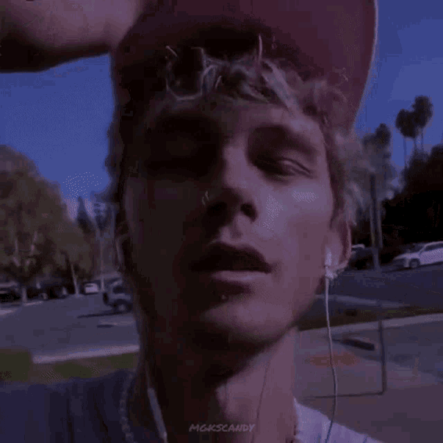 a man wearing a pink hat and ear buds is standing on a sidewalk with his eyes closed .