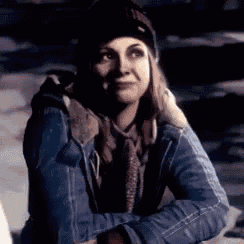 a woman wearing a blue jacket , scarf , and hat is sitting in the snow .