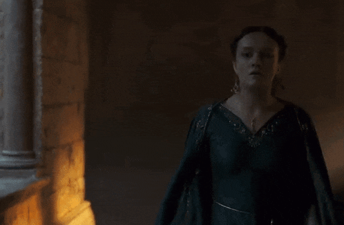 a woman in a green dress is walking in a dark hallway .