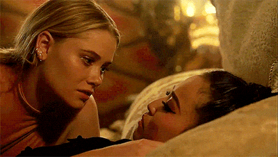 two women are laying on a bed and looking at each other