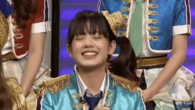 a girl in a blue uniform is smiling and holding her hair in a ponytail while standing next to other girls .