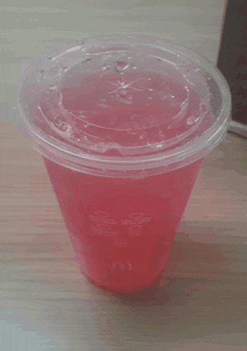 a clear plastic cup with a pink liquid in it and the letter m on it