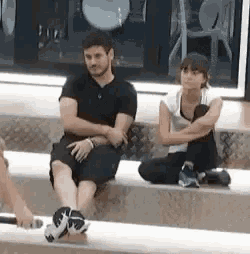 a man and a woman are sitting on a bench with their legs crossed .
